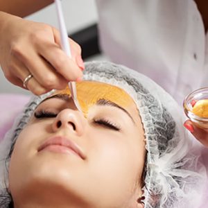 Female cosmetologist is applying gold mask to a young woman in a beauty salon. Cosmetology and skin care routine.